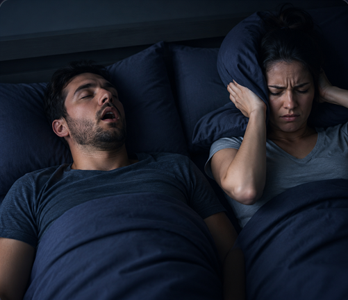 Awake partner covering ears beside a sleeping partner